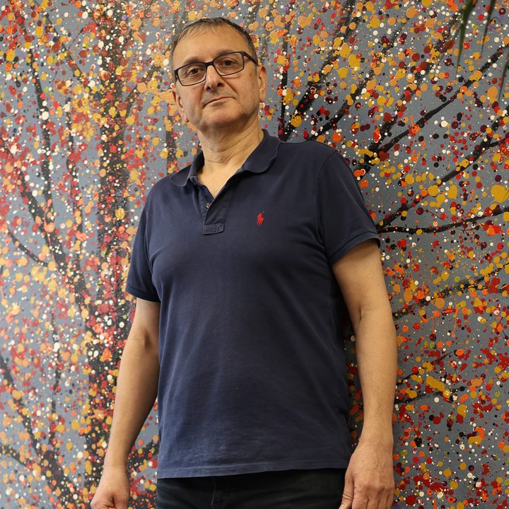 Haidar Al Shamary standing against a wall painted with a pointillist autumn tree