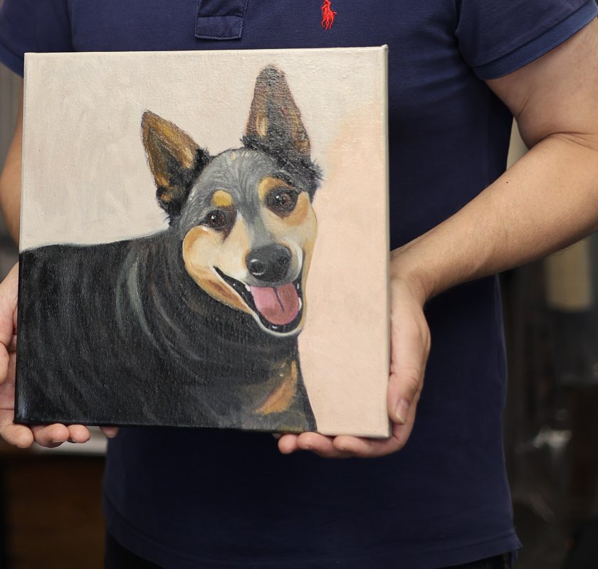 Haidar holding a painted portrait of a black and tan dog