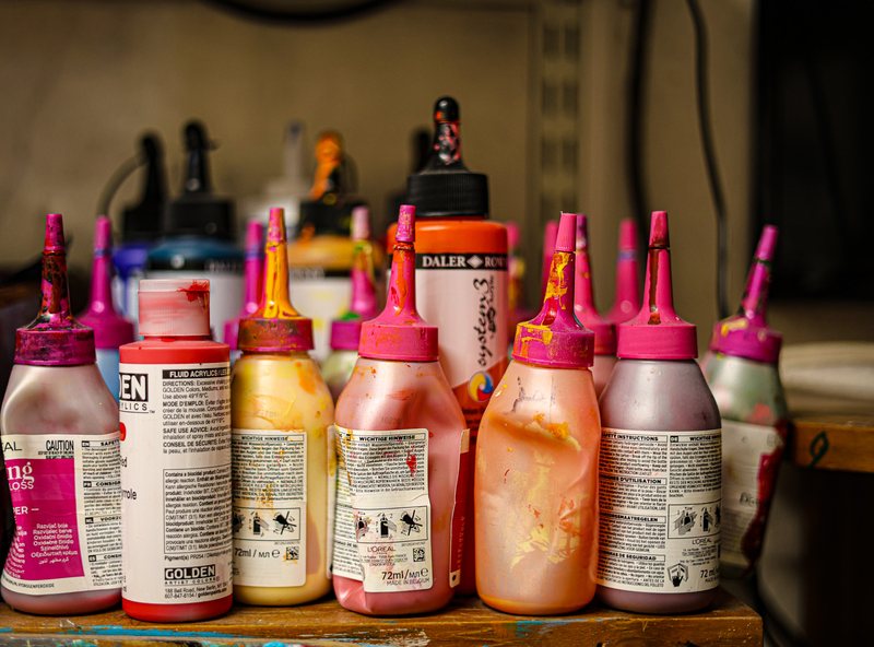 Bottles of red, pink and orange acrylic paint on a studio shelf
