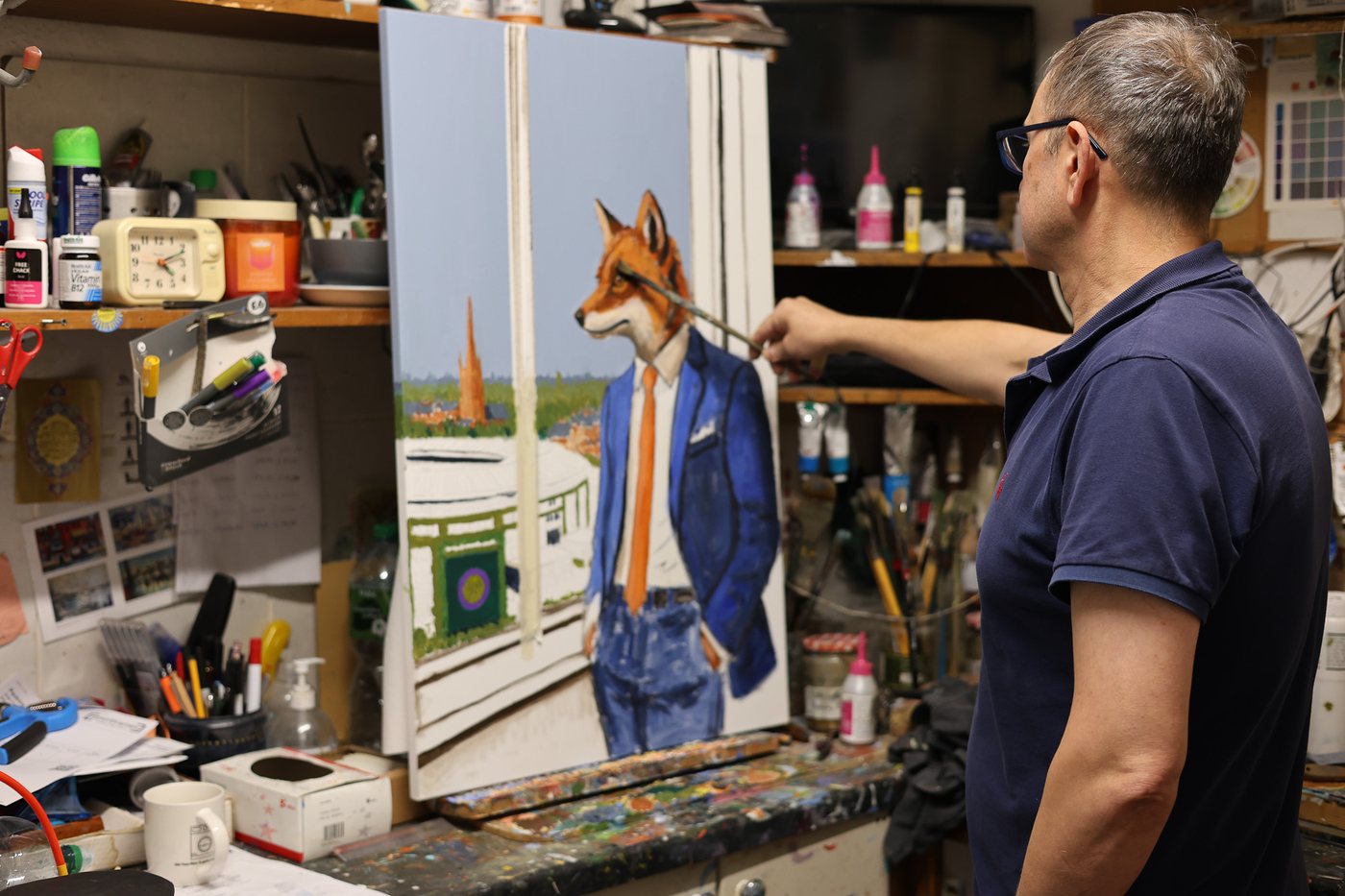 Haidar at his easel, painting a fox in a blue suit and orange tie